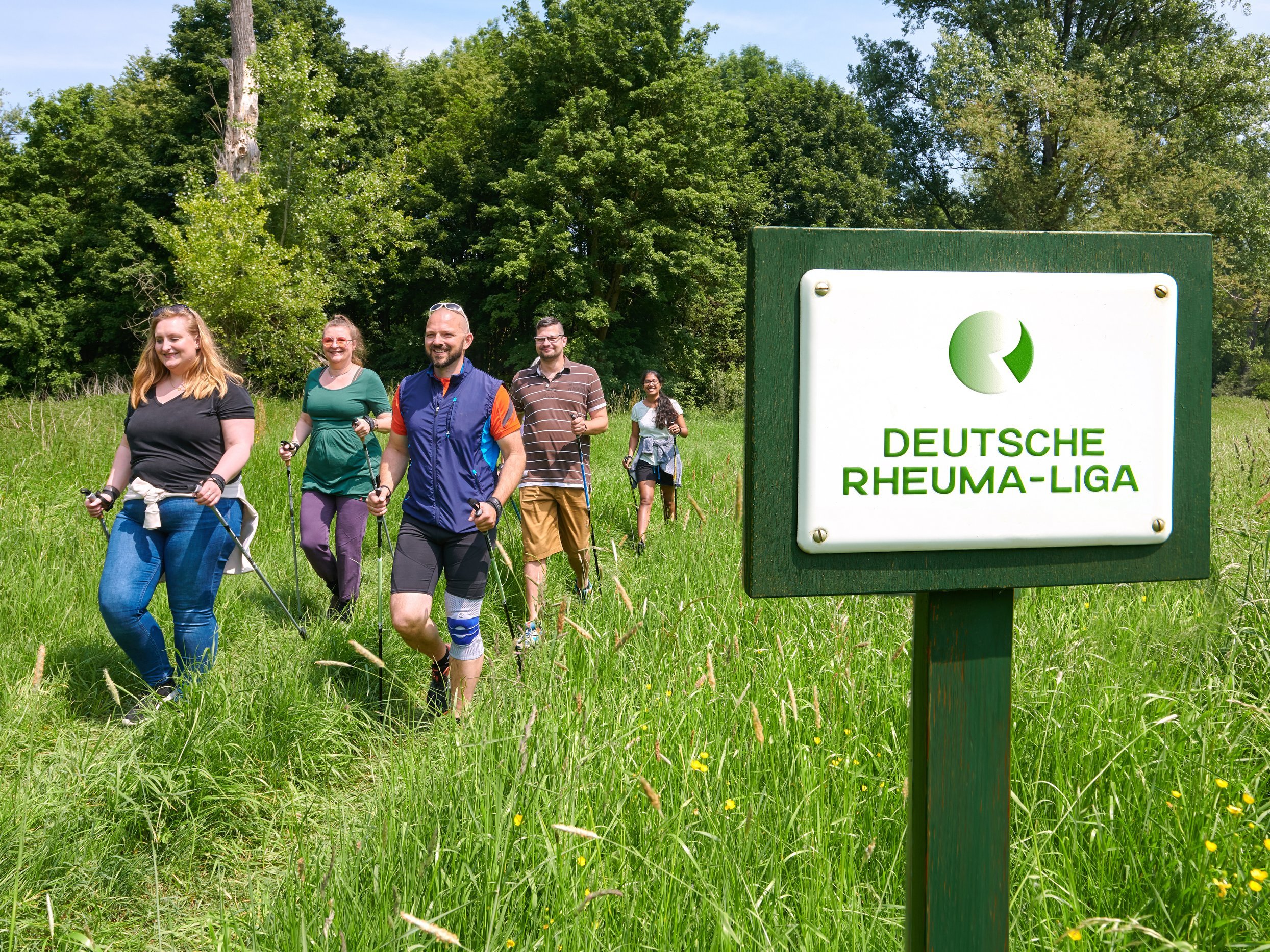 Gruppe von Menschen beim Nordic Walken, im Vordergrund Schild mit der Aufschrift "Deutsche Rheumaliga Bundesverband"