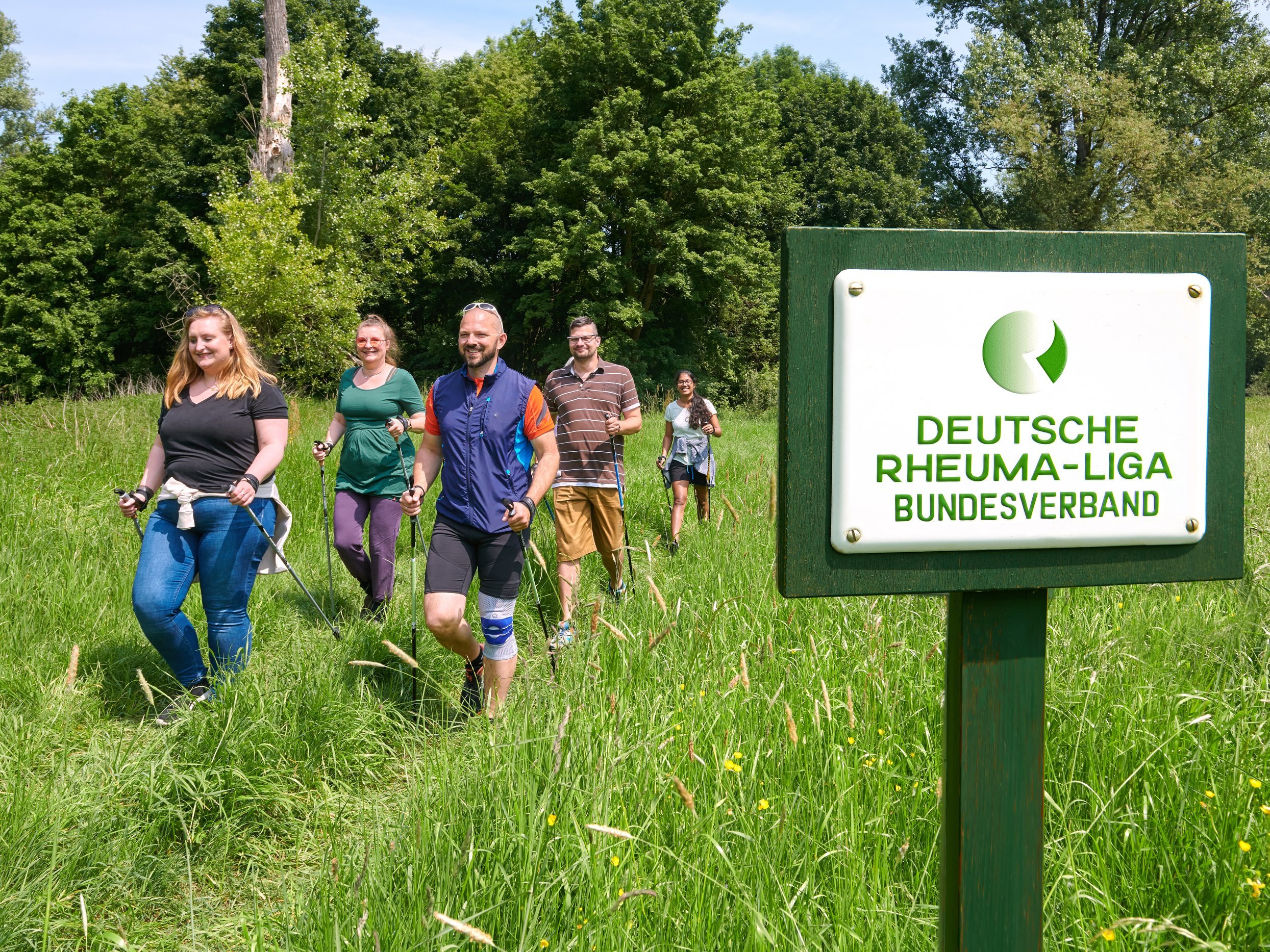 Gruppe von Menschen beim Nordic Walken, im Vordergrund Schild vom Deutschen Rheumaliga Bundesverband