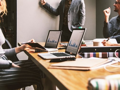 Vier Personen in Business-Kleidung stehen um einen Besprechungstisch mit Laptops